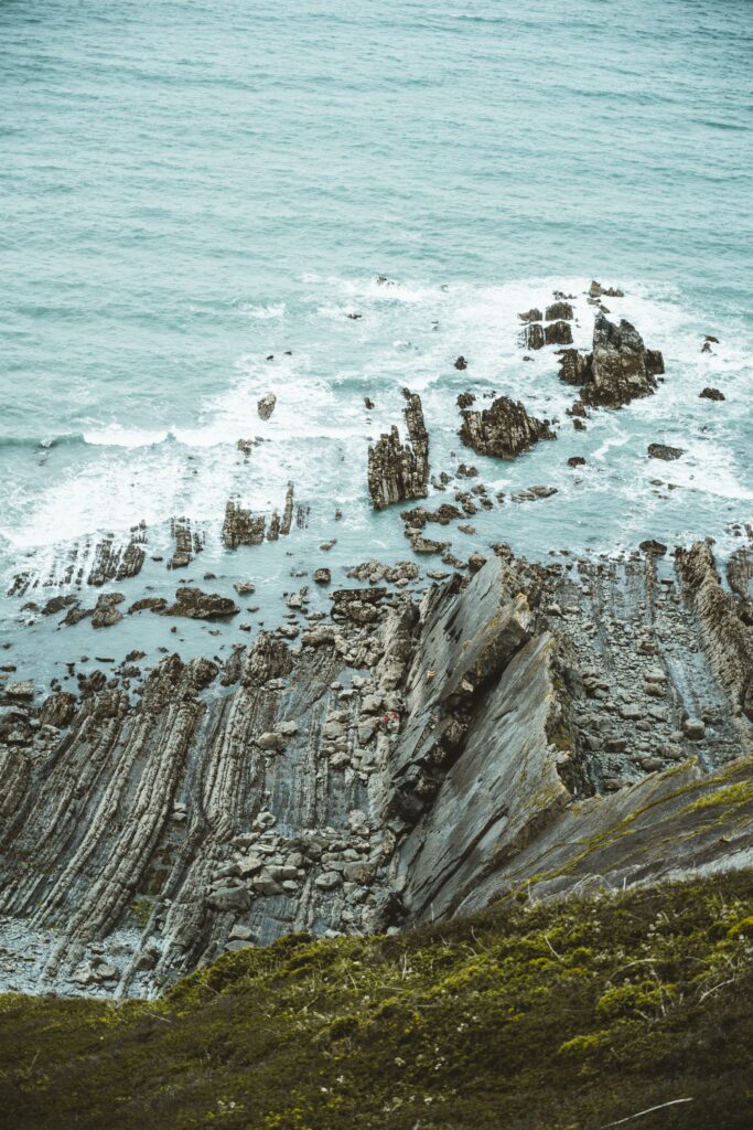 Dramatic coastal rock formations with green moss and gentle waves in natural tones wallpaper background