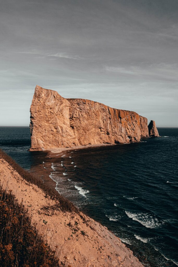 Rugged coastal rocks by deep blue sea with gentle surf and muted sky serene landscape wallpaper