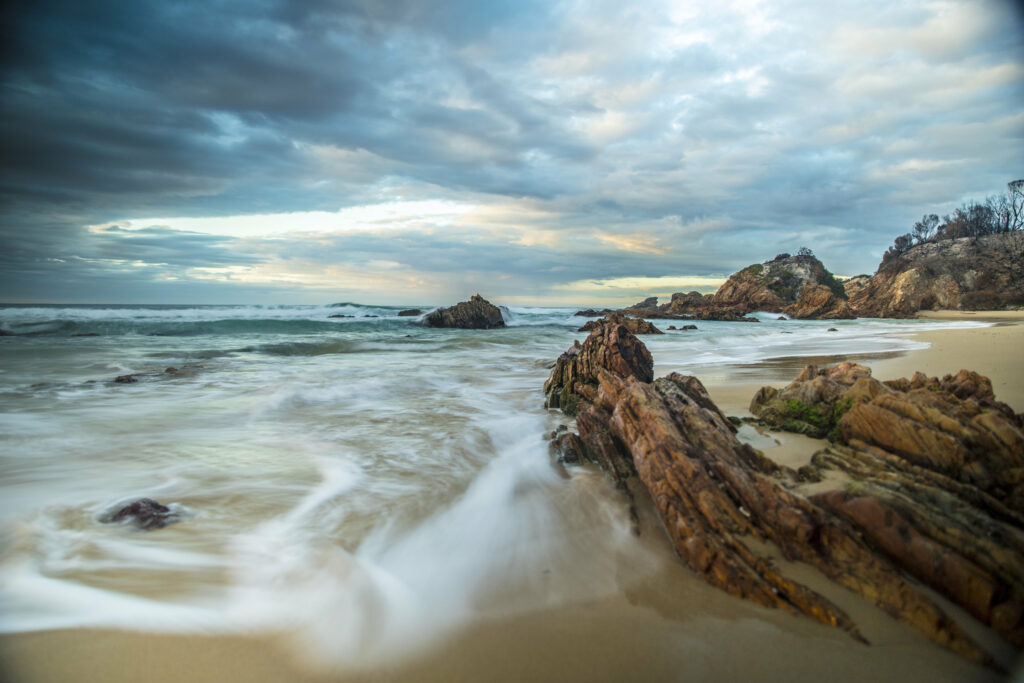 Dramatic coastal wallpaper with rugged rocks sandy beach gentle waves and moody cloudy sky