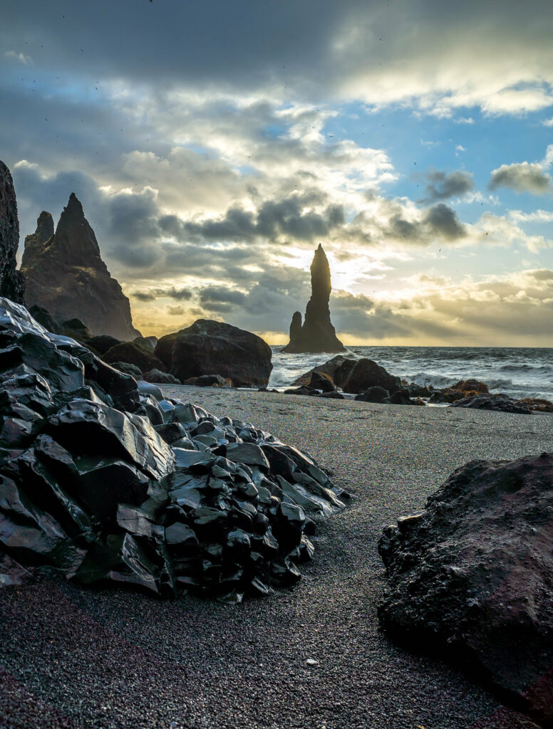 Dramatic coastal rocks and dark stones on rugged shore with turbulent sea and glowing sky wallpaper