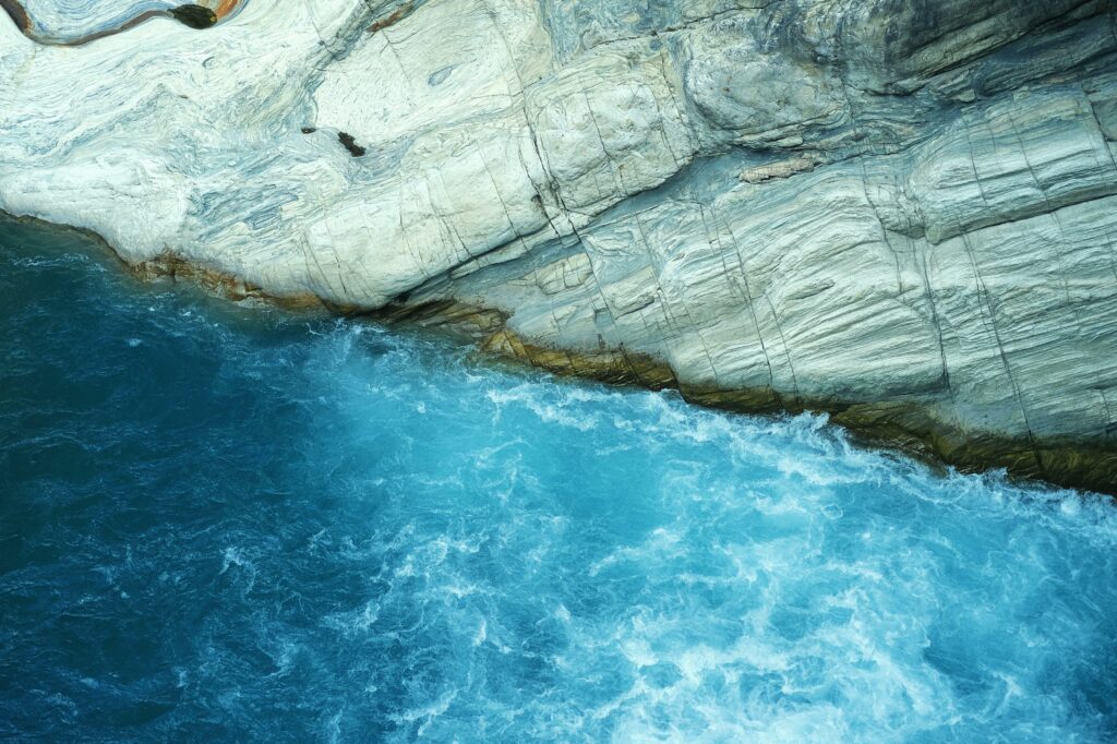 Dramatic coastal rocks with vibrant blue sea waves creating a dynamic natural wallpaper background