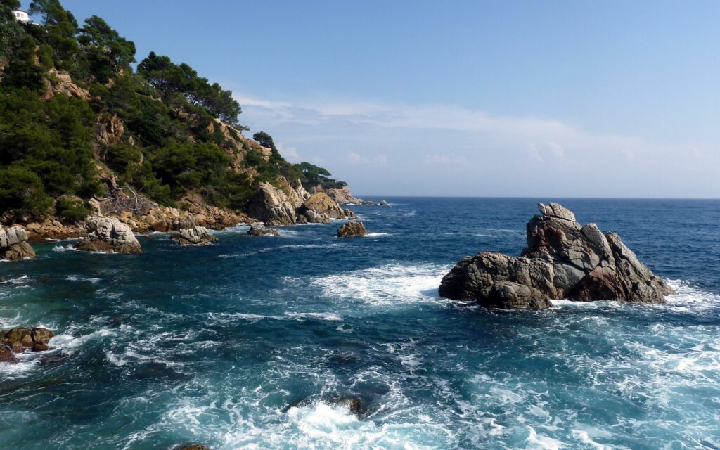 Dramatic rugged rocky coastline with crashing waves lush cliffs and clear blue ocean horizon wallpaper