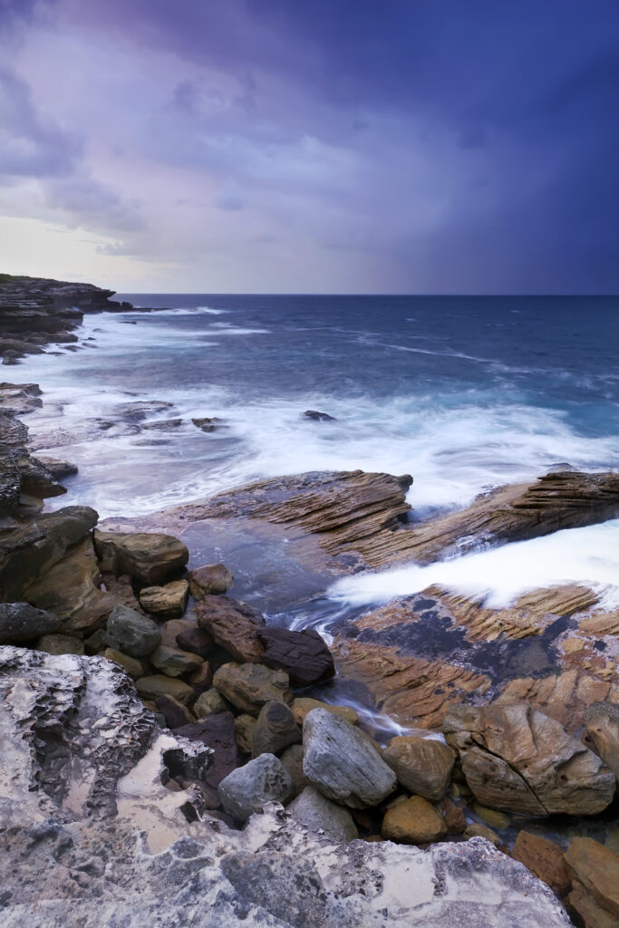Rugged rocky coastline with crashing waves earth textures deep blue sea moody sky wallpaper