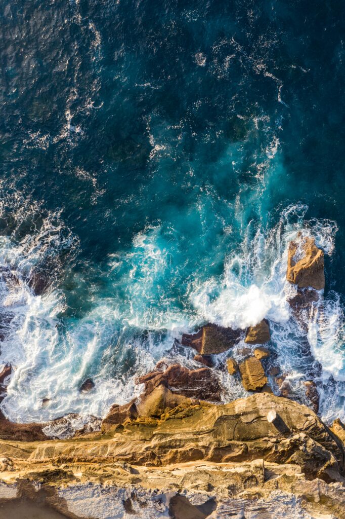 Aerial view of rugged coastal rocks with powerful ocean waves creating white foam splashes Wallpaper