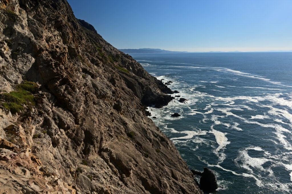 Dramatic coastal landscape with rugged rocky slopes and vibrant blue sea under clear sky wallpaper