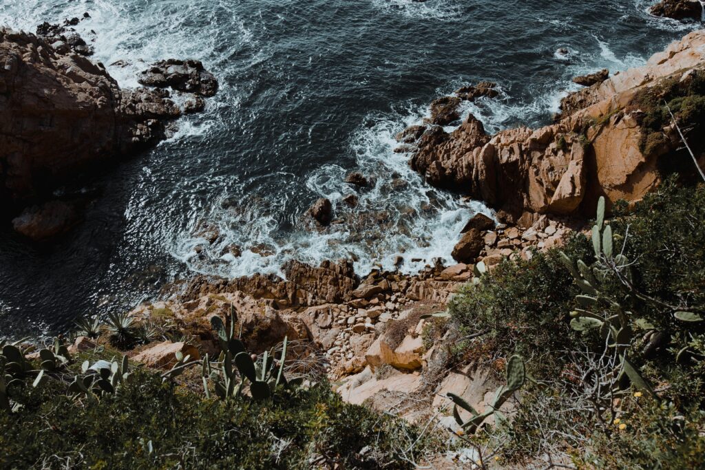 Dramatic coastal scene with rugged rocks waves crashing deep blue sea and cacti cliffs wallpaper