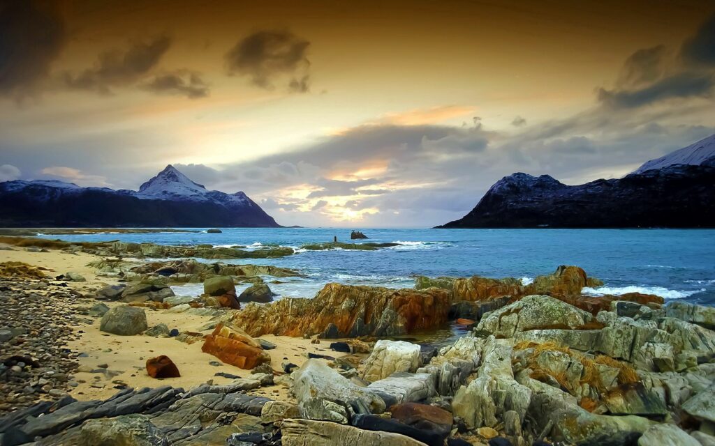 Dramatic coastal seascape with rugged rocks vibrant blue sea and vivid sunset sky wallpaper