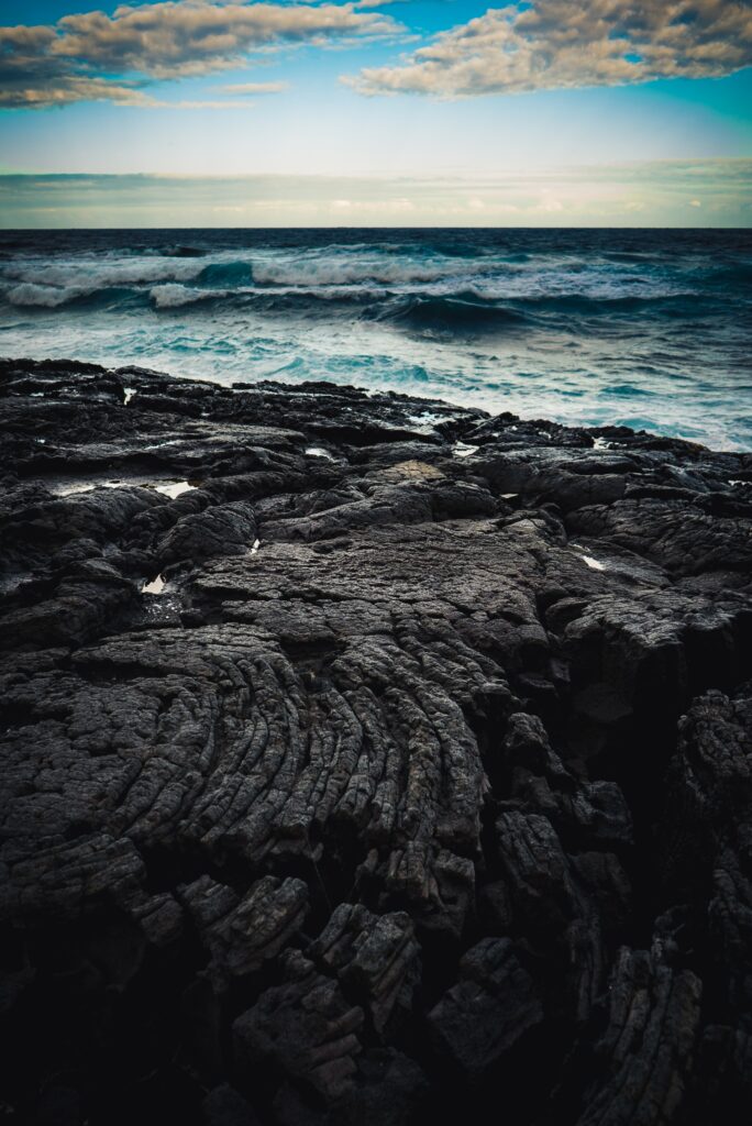 Dramatic rugged coastal rocks with crashing waves under vibrant blue sky seascape wallpaper background