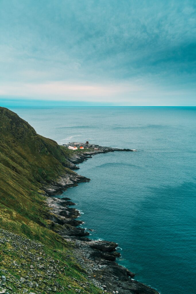 Dramatic rocky coastal slope with quaint seaside buildings calm blue sea and cloud-streaked sky wallpaper