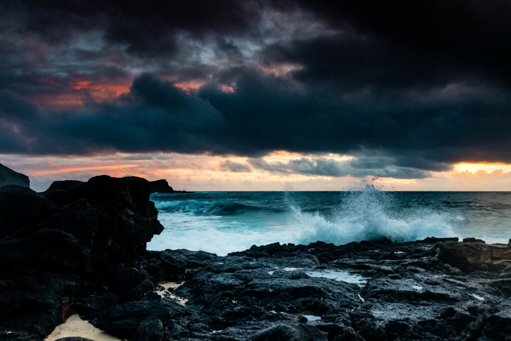 Dramatic clouds over rugged volcanic coastline with powerful waves and glowing horizon sea view Wallpaper