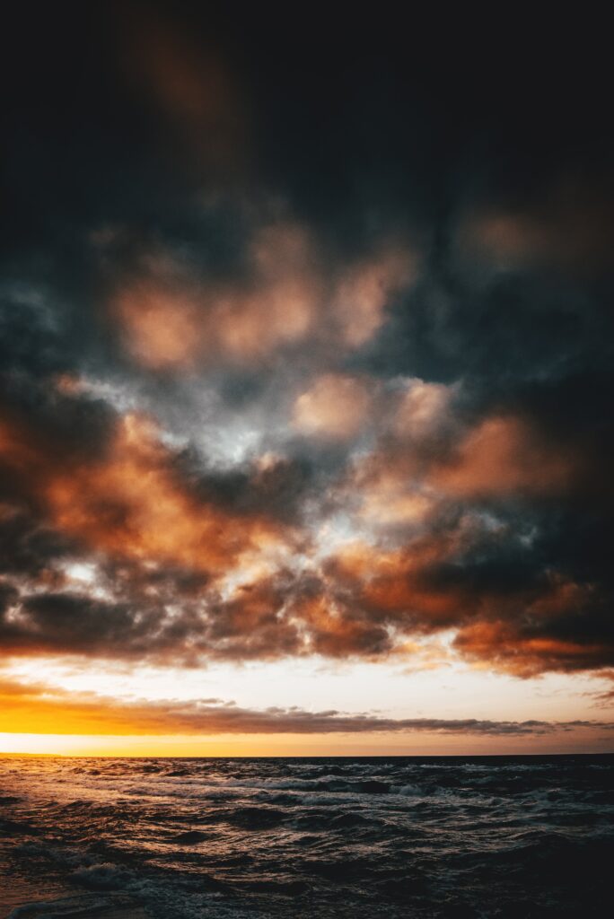Dramatic coastal wallpaper with dark sea waves vivid orange sunset and moody gray clouds