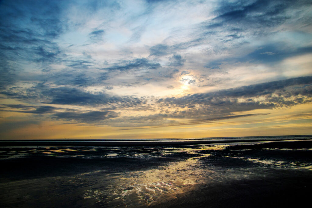Dramatic coastal sunset with dark moody clouds reflecting on wet sand sea shore wallpaper background