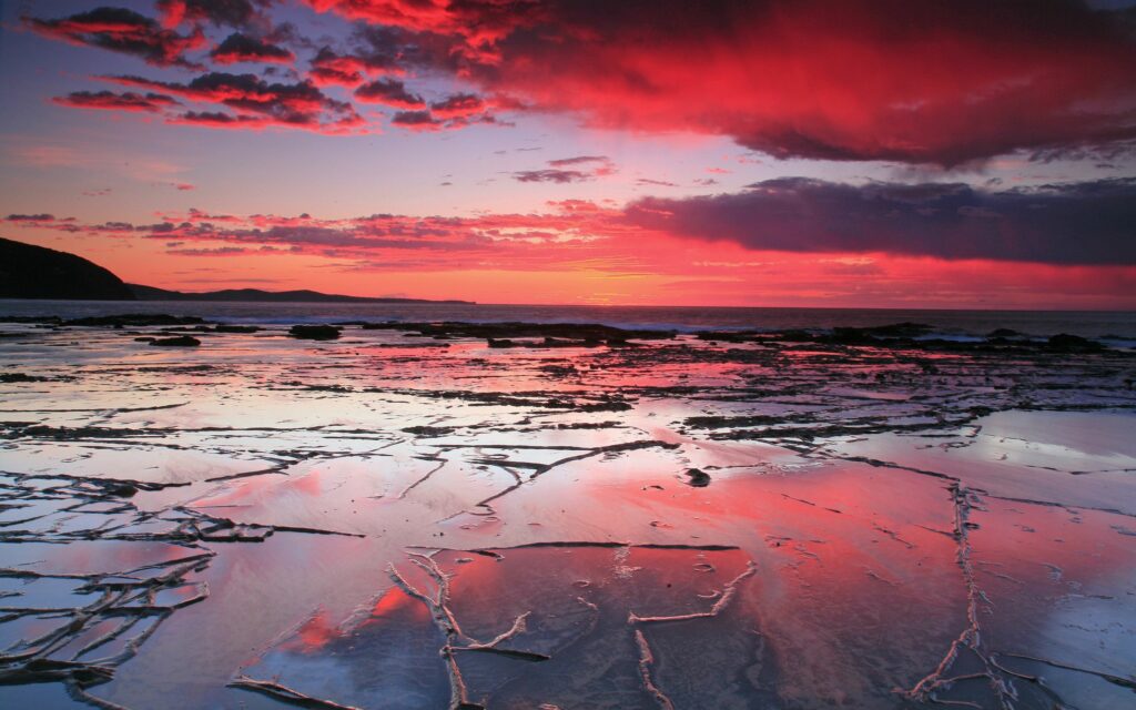 Sunset coastal landscape with intricate sand patterns reflecting red pink sky on wet shore Wallpaper