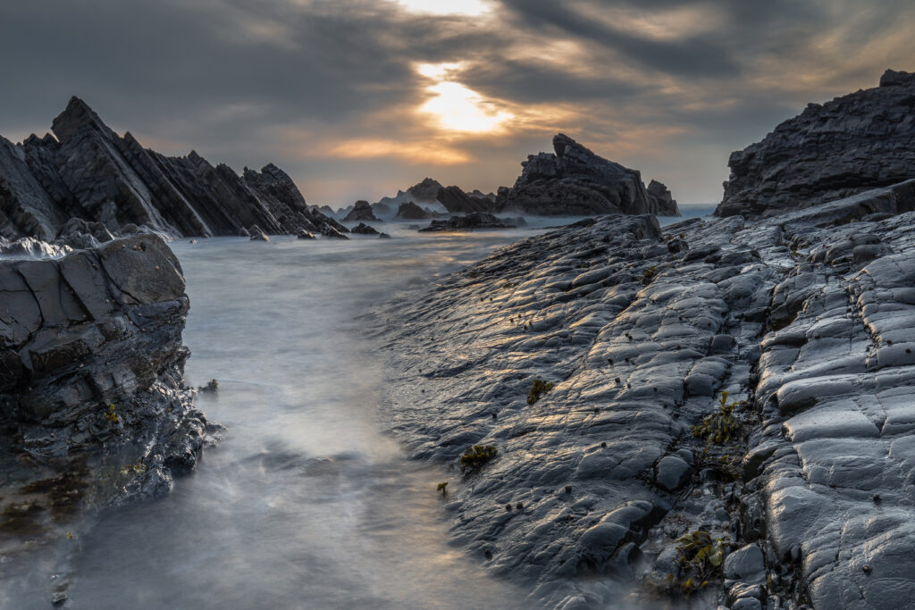 Dramatic coastal landscape with jagged rocks and silky water under golden sunset sky wallpaper
