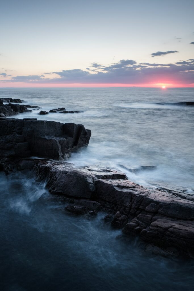 Dramatic coastal wallpaper with rugged rocks and waves under vibrant pastel sunset horizon