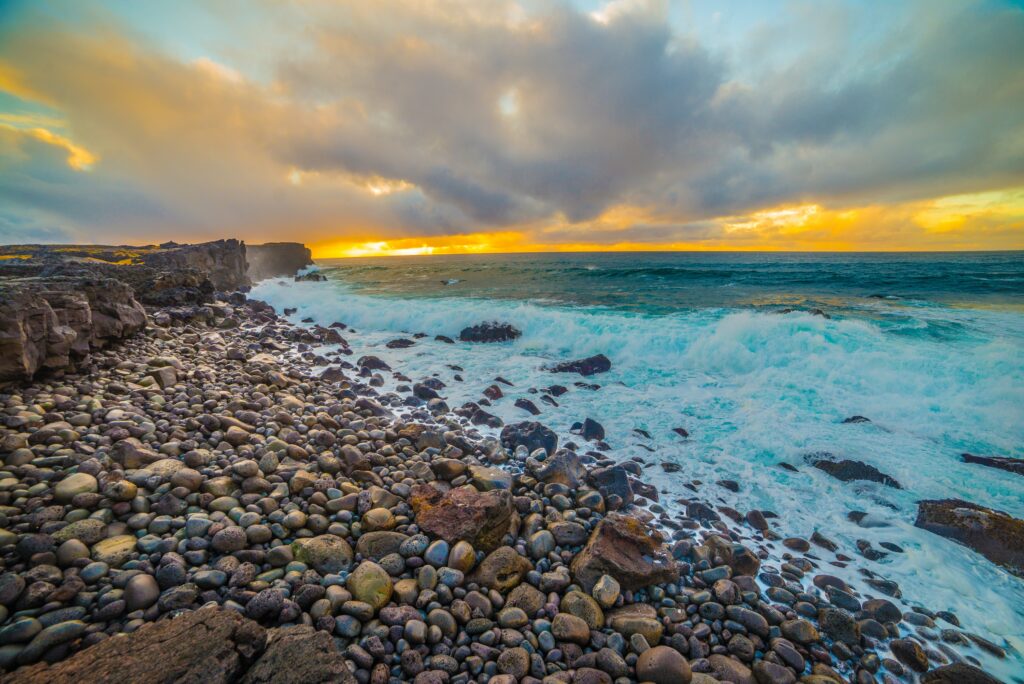 Dramatic coastal wallpaper with smooth stones waves crashing vibrant yellow blue orange sunset
