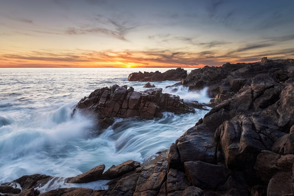 Dramatic coastal rocks with surging waves under vibrant sunset sky perfect sea wallpaper background