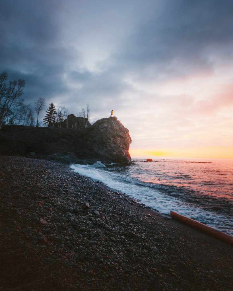 Dramatic coastal rock formation sunset waves stone beach sparse trees tranquil landscape wallpaper