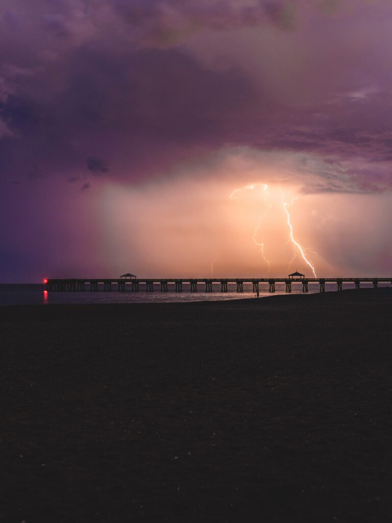 Dramatic coastal thunderstorm with lightning over pier under dark purple storm clouds wallpaper background