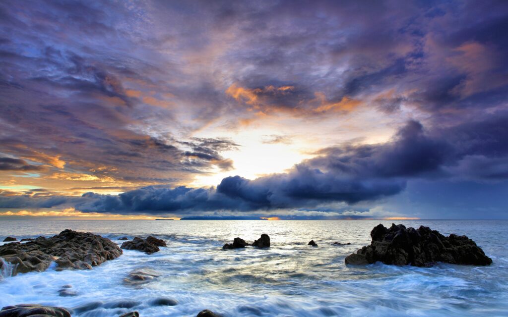 Dramatic coastal wallpaper with rugged stones waves under colorful cloudy sky serene seascape