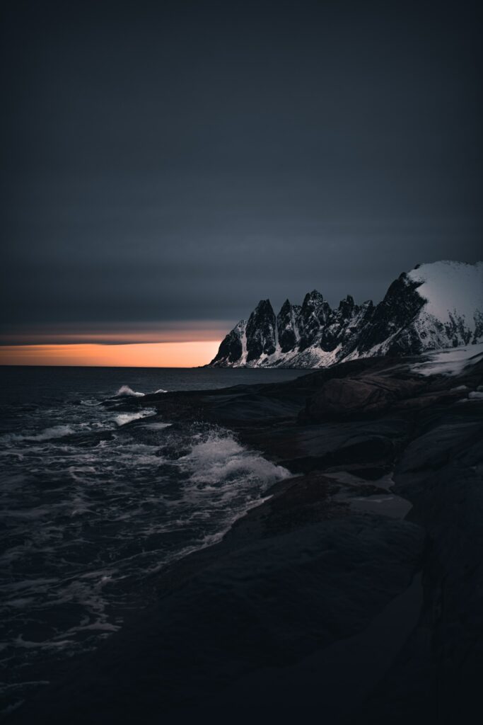 Dramatic coastal wallpaper with jagged snow-capped mountains rugged rocks and crashing waves