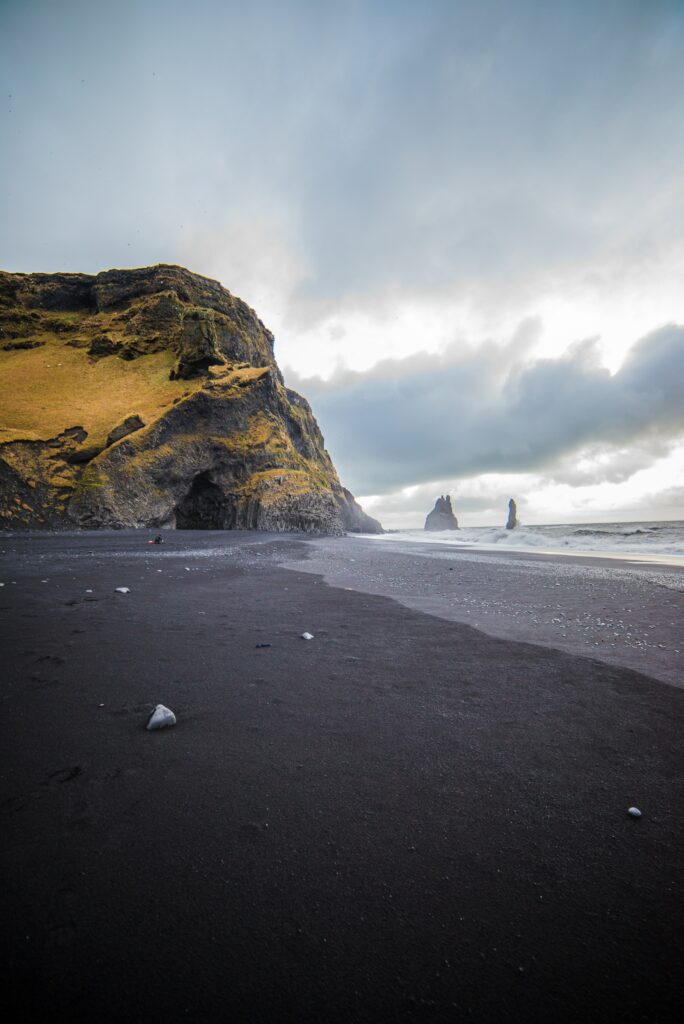 Dramatic coastal scene with dark sand white stones crashing waves rugged cliffs golden moss Wallpaper