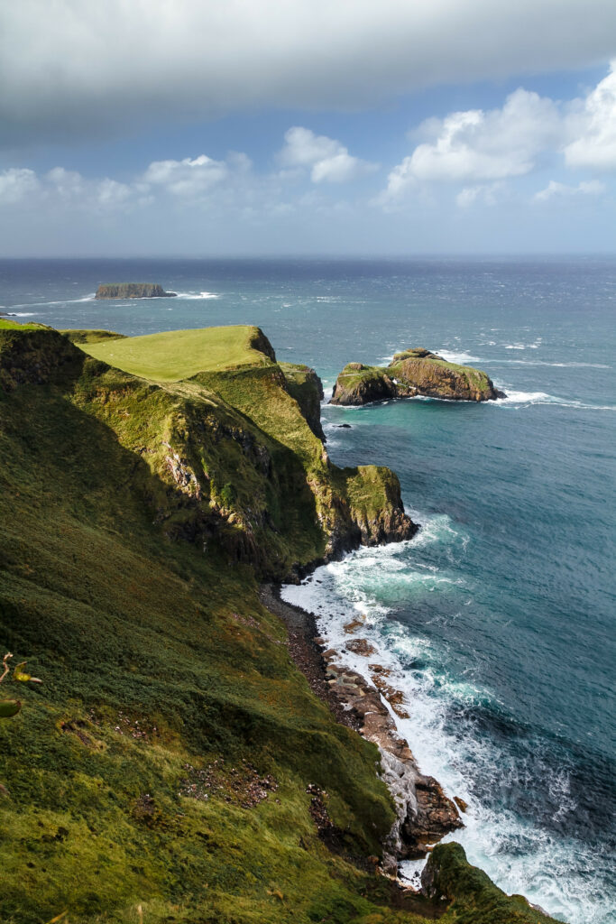 Dramatic coastal wallpaper with steep grassy cliffs rugged rocks vibrant blue sea and white surf