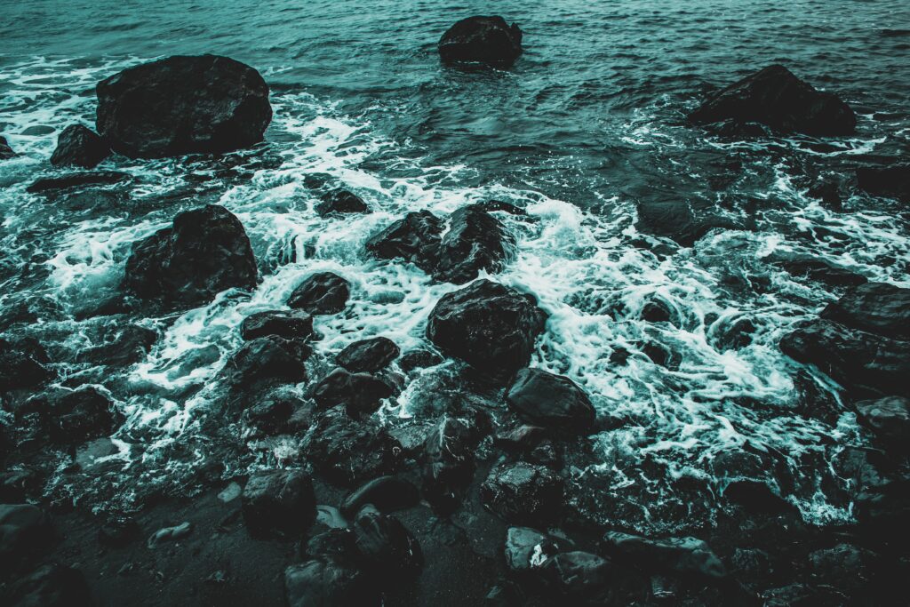 Dramatic ocean waves crashing on dark rocky shore with blue and teal tones wallpaper background