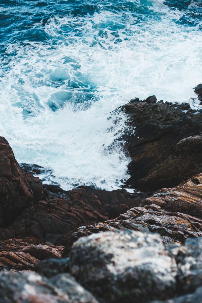 Powerful ocean waves crash on rugged brown coastal rocks with foamy white water splash wallpaper