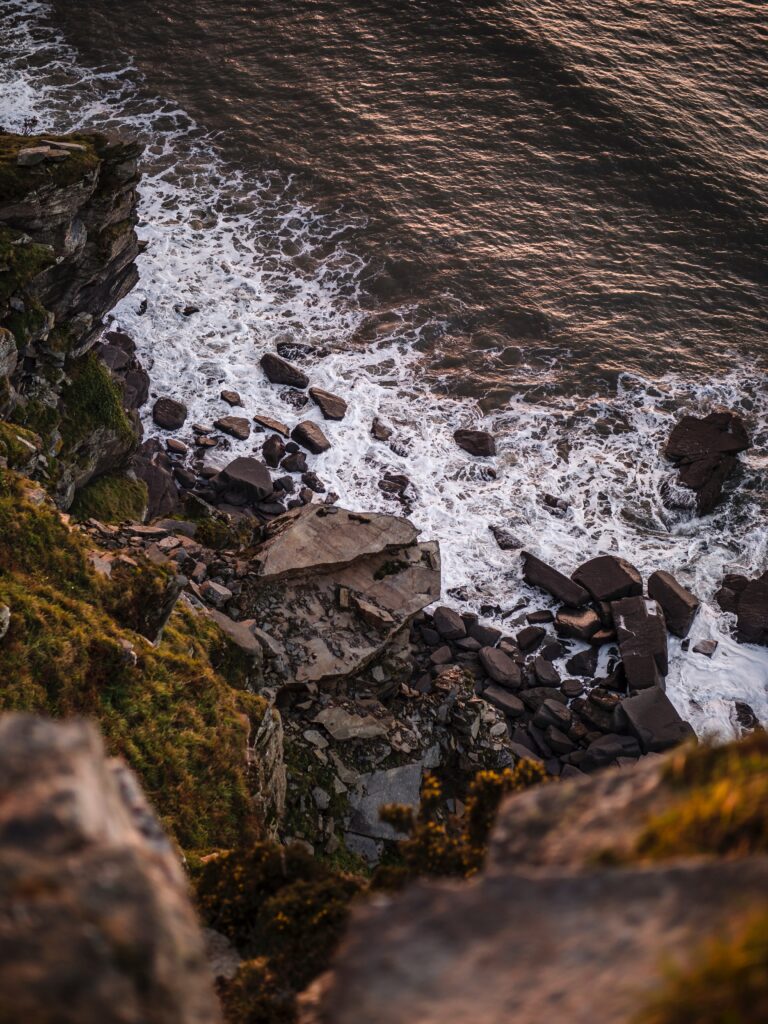Dramatic coastal waves crashing on rugged rocks with foamy sea and warm natural light wallpaper