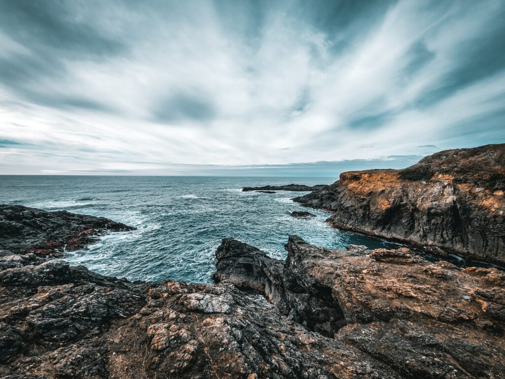 Dramatic coastal scene with rugged rocks crashing waves turquoise sea and moody cloudy sky wallpaper