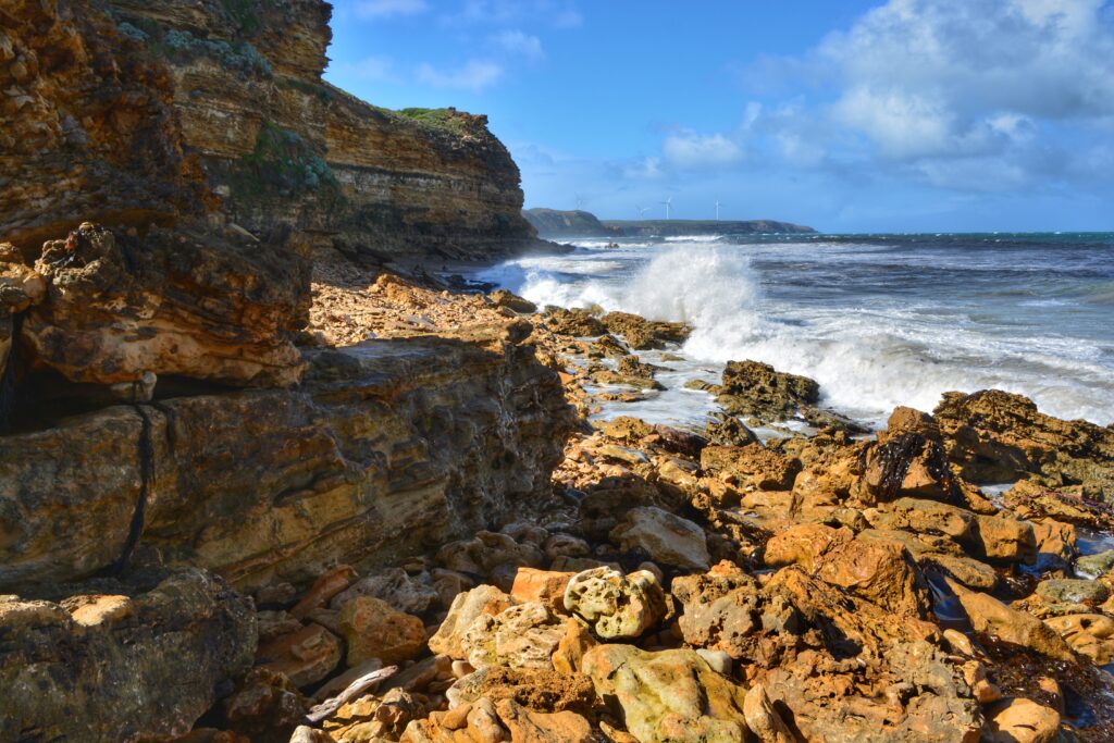 Vibrant coastal scene with rugged rocks and crashing sea waves under bright blue sky wallpaper