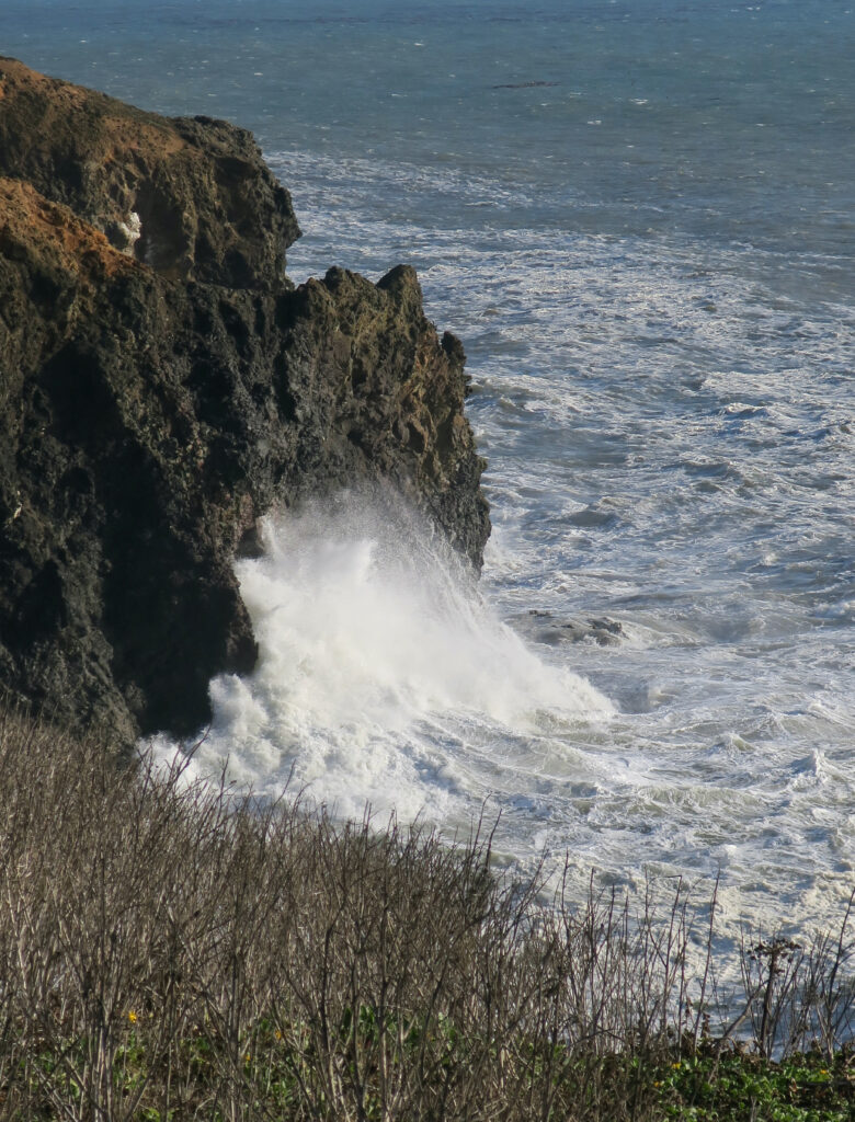 Dramatic waves crashing on rugged coastal rocks under cloudy sky with deep blue ocean backdrop Wallpaper
