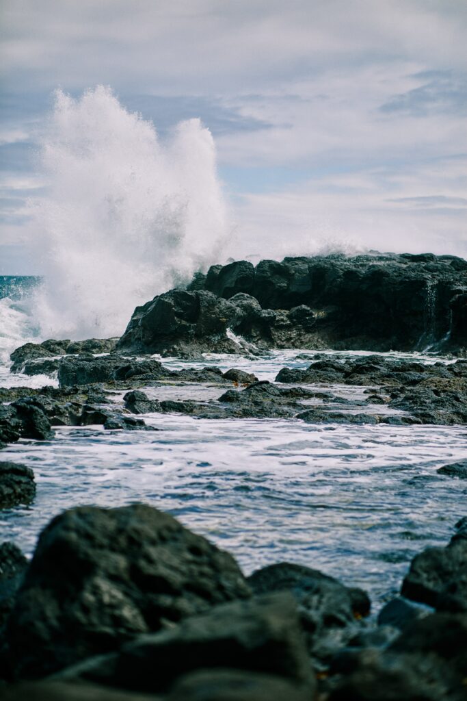 Powerful ocean waves crash on rugged rocks under cloudy sky coastal wallpaper background
