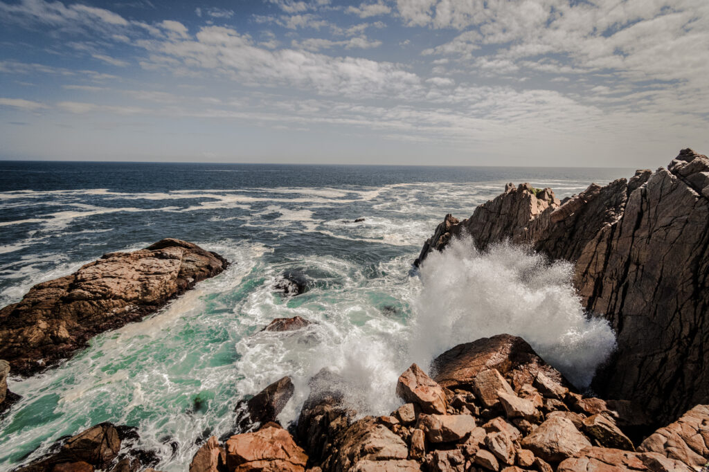 Dynamic ocean waves crash on rugged rocks under a partly cloudy sky coastal wallpaper background