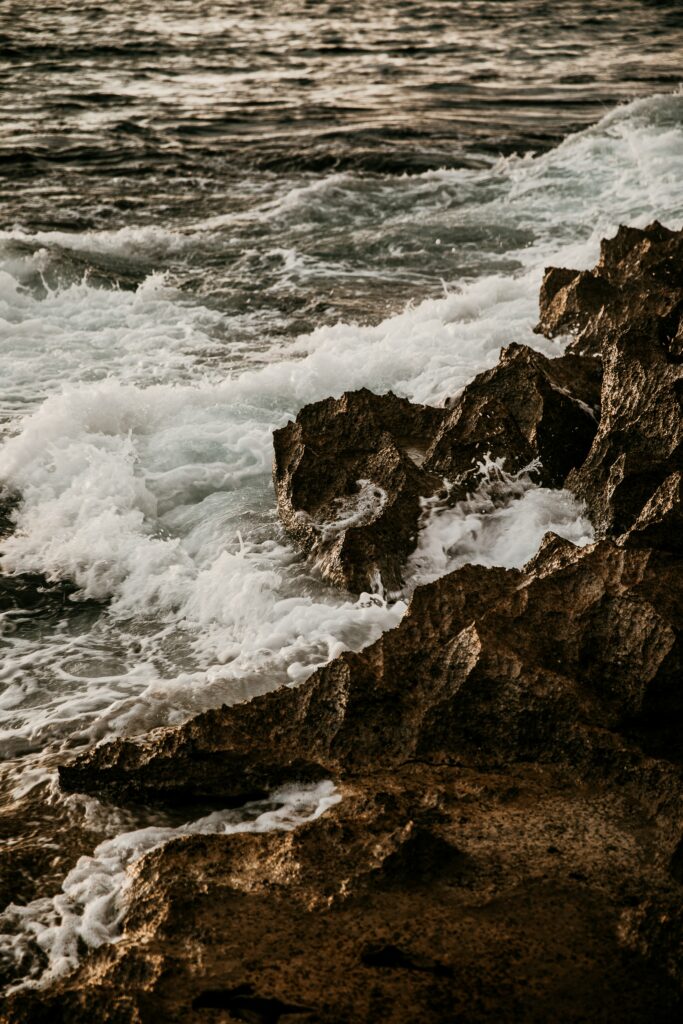 Dynamic ocean waves crash on rugged rocks with golden light foamy water coastal wallpaper