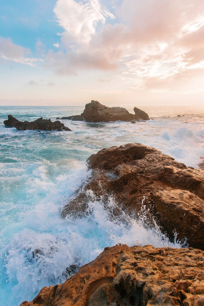 Dramatic coastal waves crashing on rugged rocks under vibrant colorful sky wallpaper background