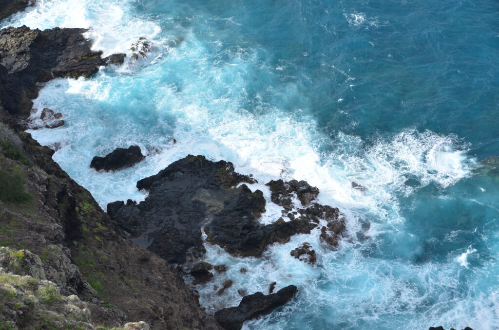 Powerful ocean waves crash on rugged rocky coastline creating white sea foam and blue water Wallpaper