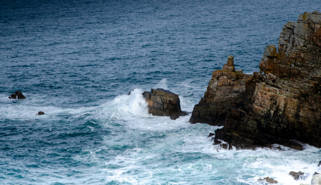 Dynamic ocean waves crash on rugged rocky cliffs with deep blue water and earthy tones background Wallpaper