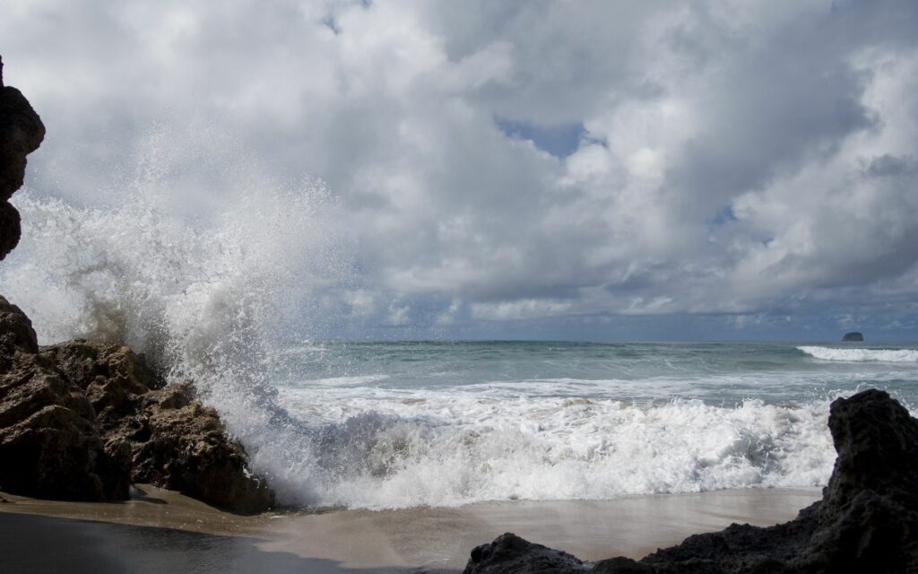 Dramatic coastal wallpaper with powerful ocean waves crashing rugged stones under cloudy sky