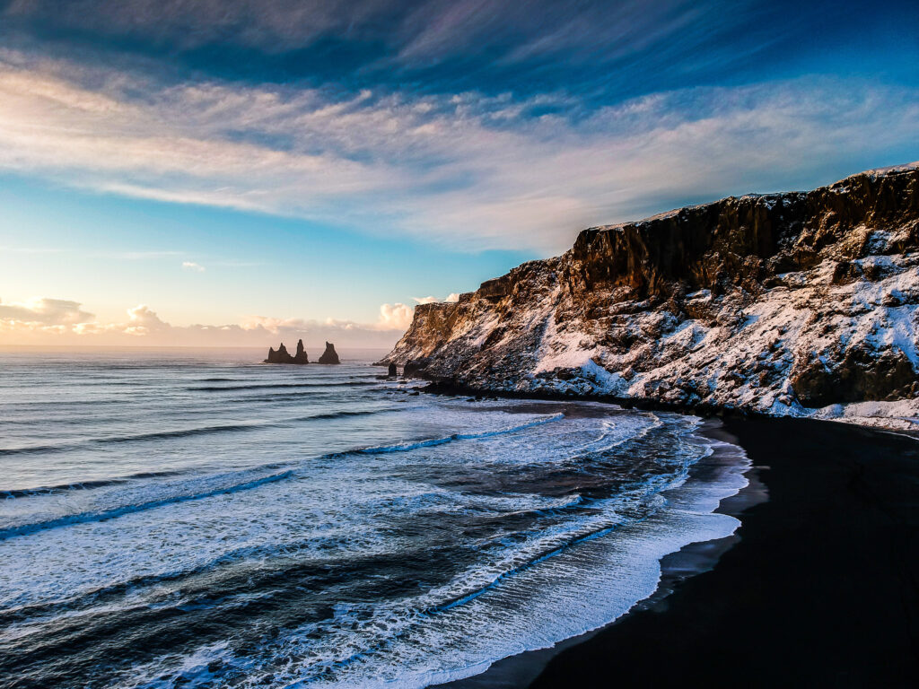Dramatic coastal wallpaper with crashing waves dark rocks snowcapped cliffs and pastel sky