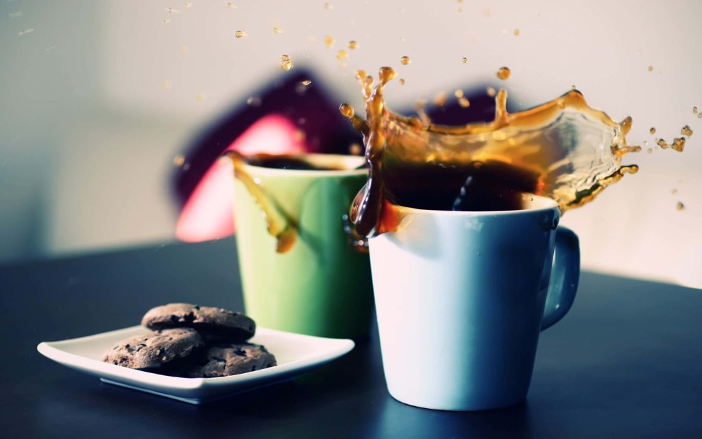 High-speed splash from white coffee mug with green mug and chocolate chip cookies on dark surface Wallpaper