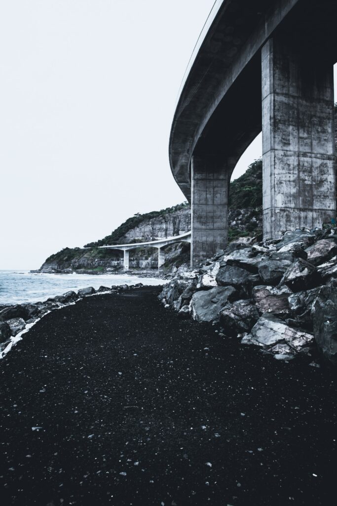 Curved modern concrete bridge over rocky cliffs by turbulent sea with dramatic coastal landscape view Wallpaper