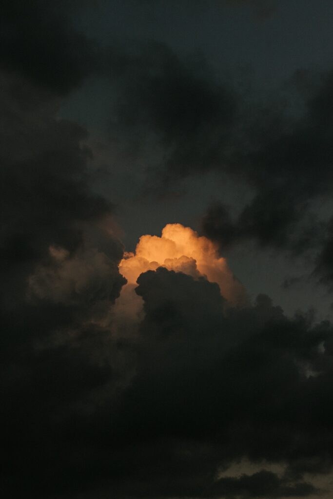 Dramatic stormy sky with dark clouds and warm golden sunlight breaking through wallpaper background