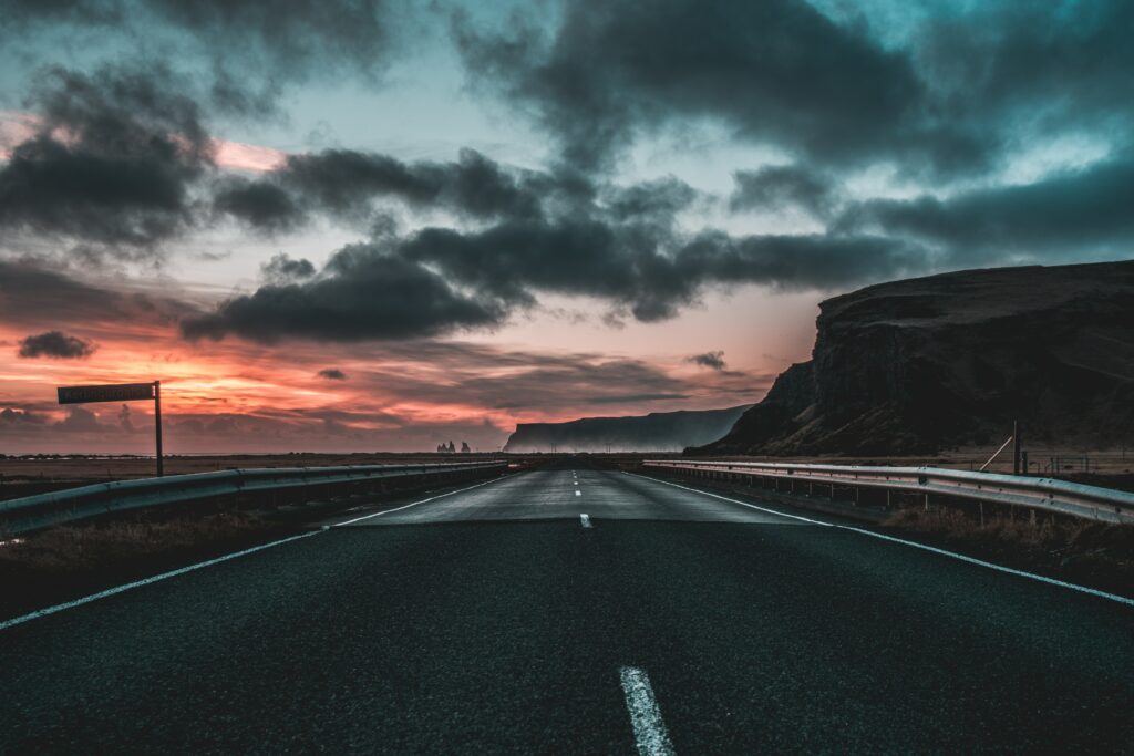 Open road at dawn with white markings rugged cliffs and dramatic clouds in moody orange blue tones Wallpaper