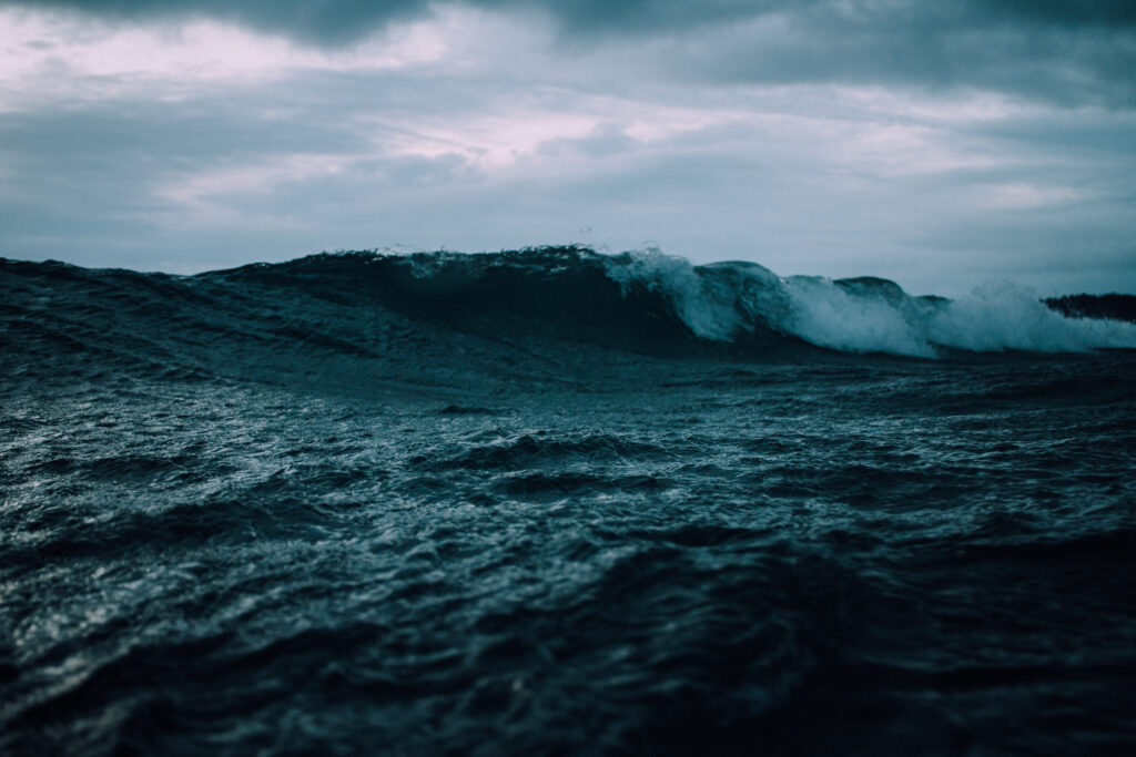 Dramatic deep blue ocean waves roll under a moody cloudy sky seascape wallpaper background