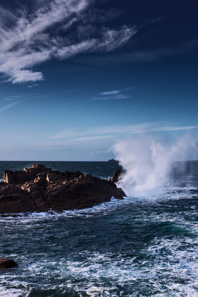 Dramatic seascape wallpaper with deep blue waves crashing rugged rocks under vibrant sky