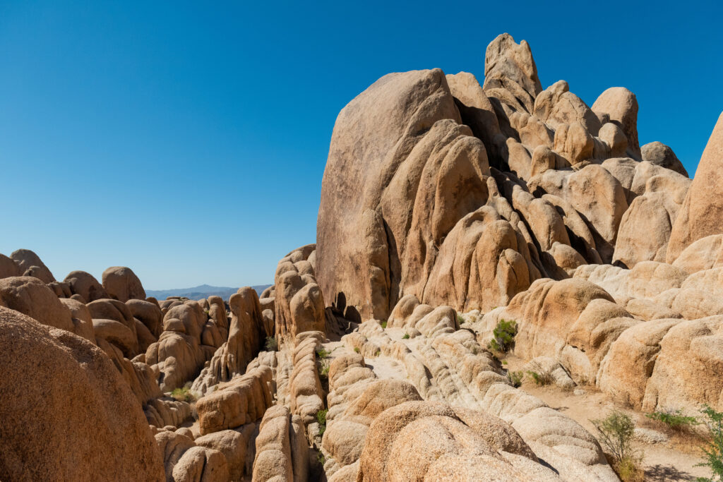 Sunlit rugged rock formations with natural reliefs and green bushes under clear blue sky wallpaper