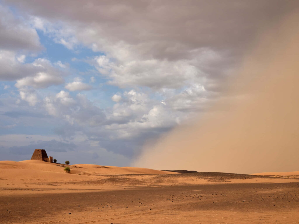 Dramatic desert landscape with golden sand dunes dusty storm ancient stone structure wallpaper background