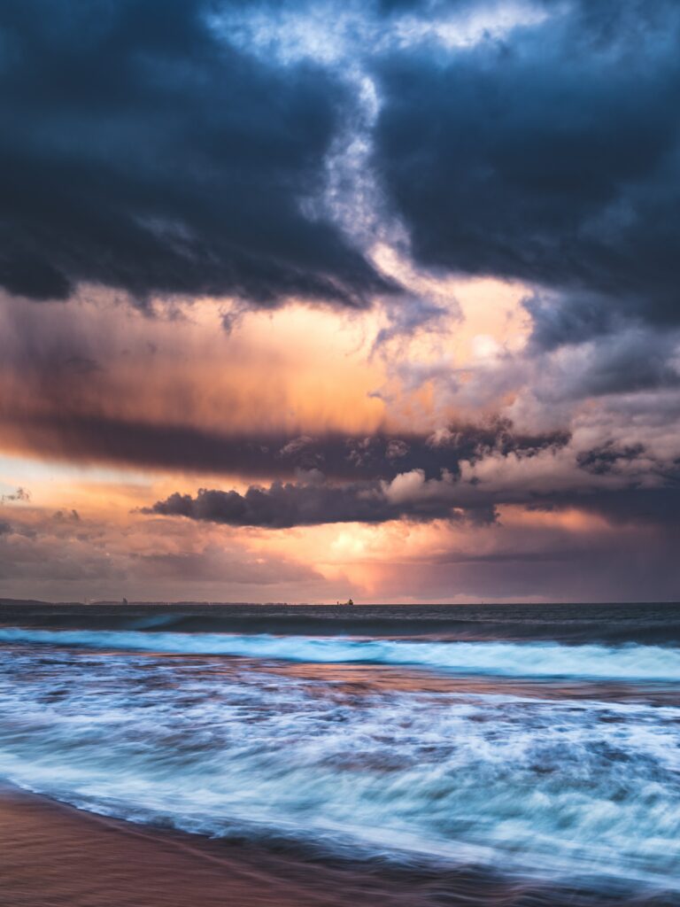Dramatic dusk seascape wallpaper with vibrant crashing waves and dynamic sunset clouds background
